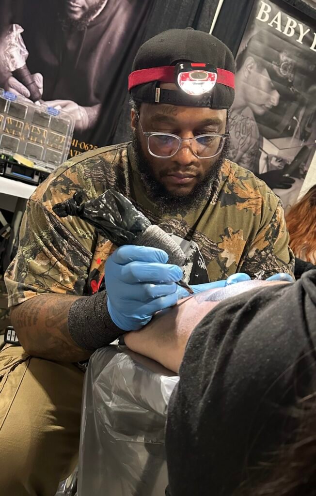 Dom Wilkes Tattoos by Dom man tattooing with rotary machine wearing glasses and blue gloves and headlamp